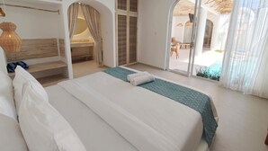 A hotel room with a large bed, a small bench, a vanity with a mirror, and a sliding glass door leading to a pool area. - Villa Chioni Uluwatu (Ungasan)