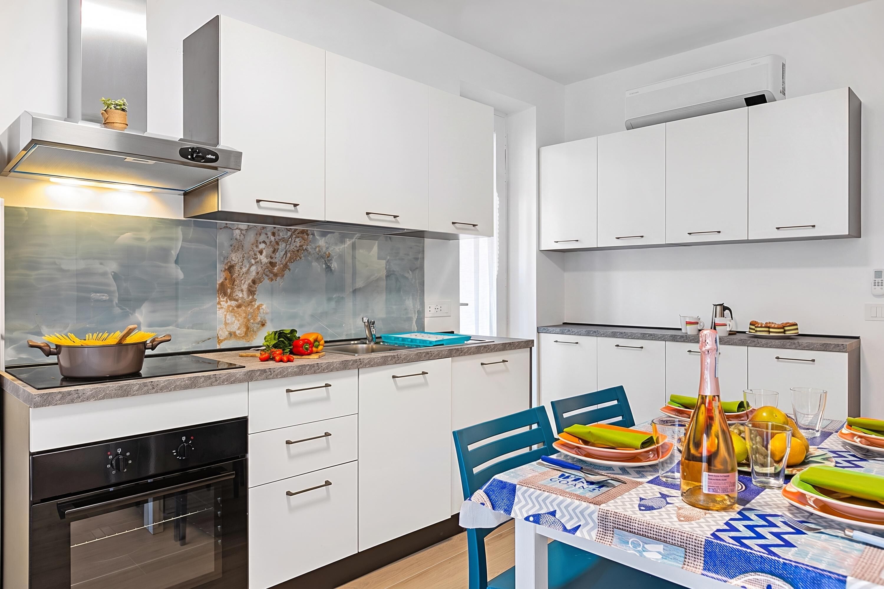 Cocina moderna con gabinetes blancos, horno empotrado y comedor con mesa lista para una comida.