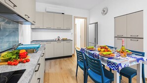 A modern kitchen with a dining area, featuring a built-in oven, a sink, and a dining table set for a meal. - Merlo A -  Center & Private Parking, Ceriale, Italy (Ceriale)