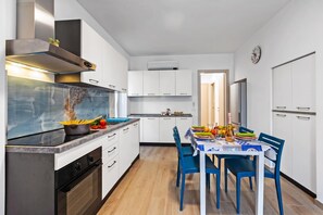 Une cuisine moderne avec des armoires blanches, une hotte en acier inoxydable et un coin repas avec des chaises bleues et une table mise pour le repas.