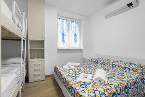 Ein Schlafzimmer mit Etagenbetten, einem Nachttisch, einem Fenster mit Vorhängen und einer Klimaanlage.