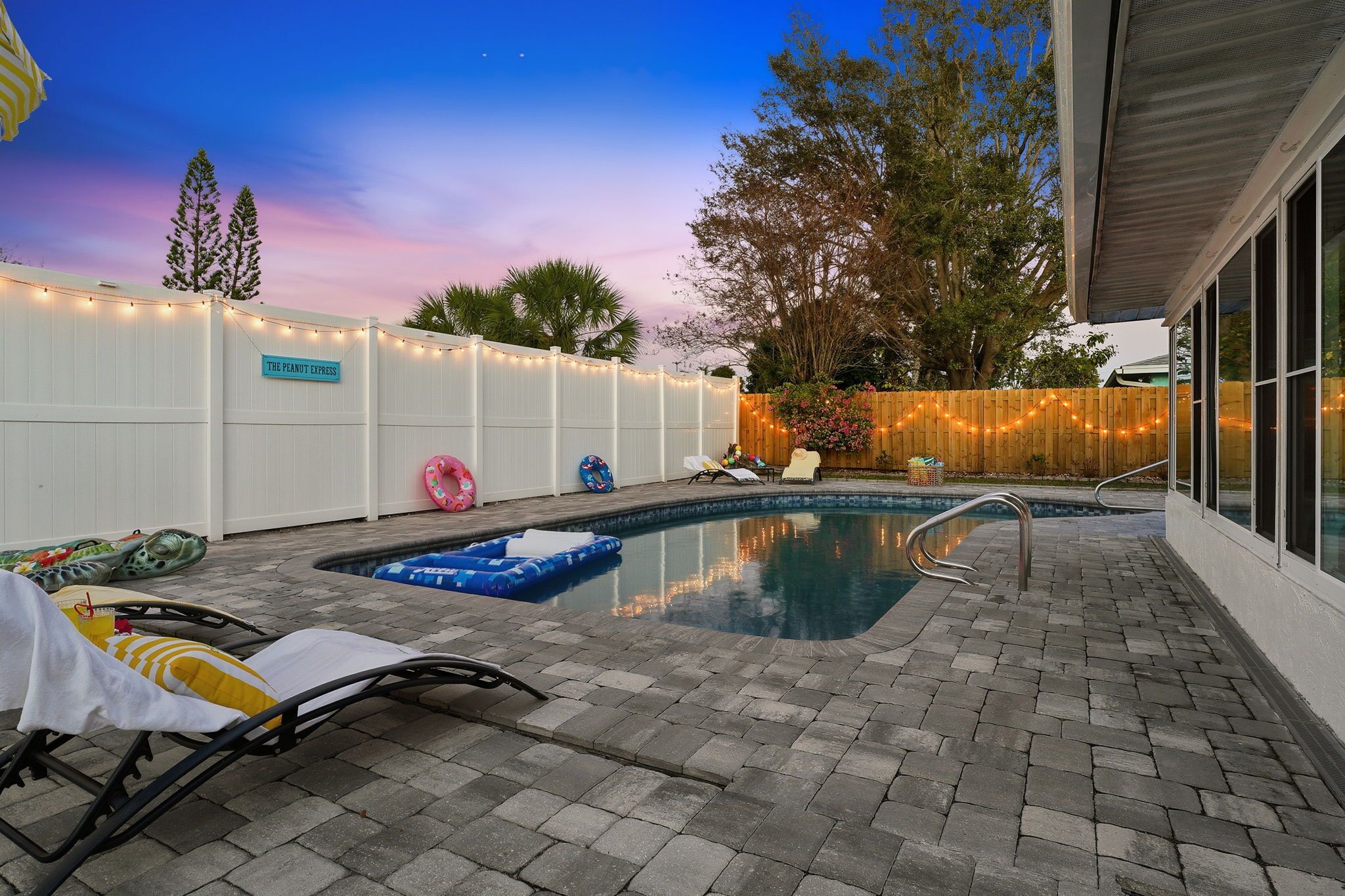 A backyard with a swimming pool, lounge chairs, and a wooden fence.