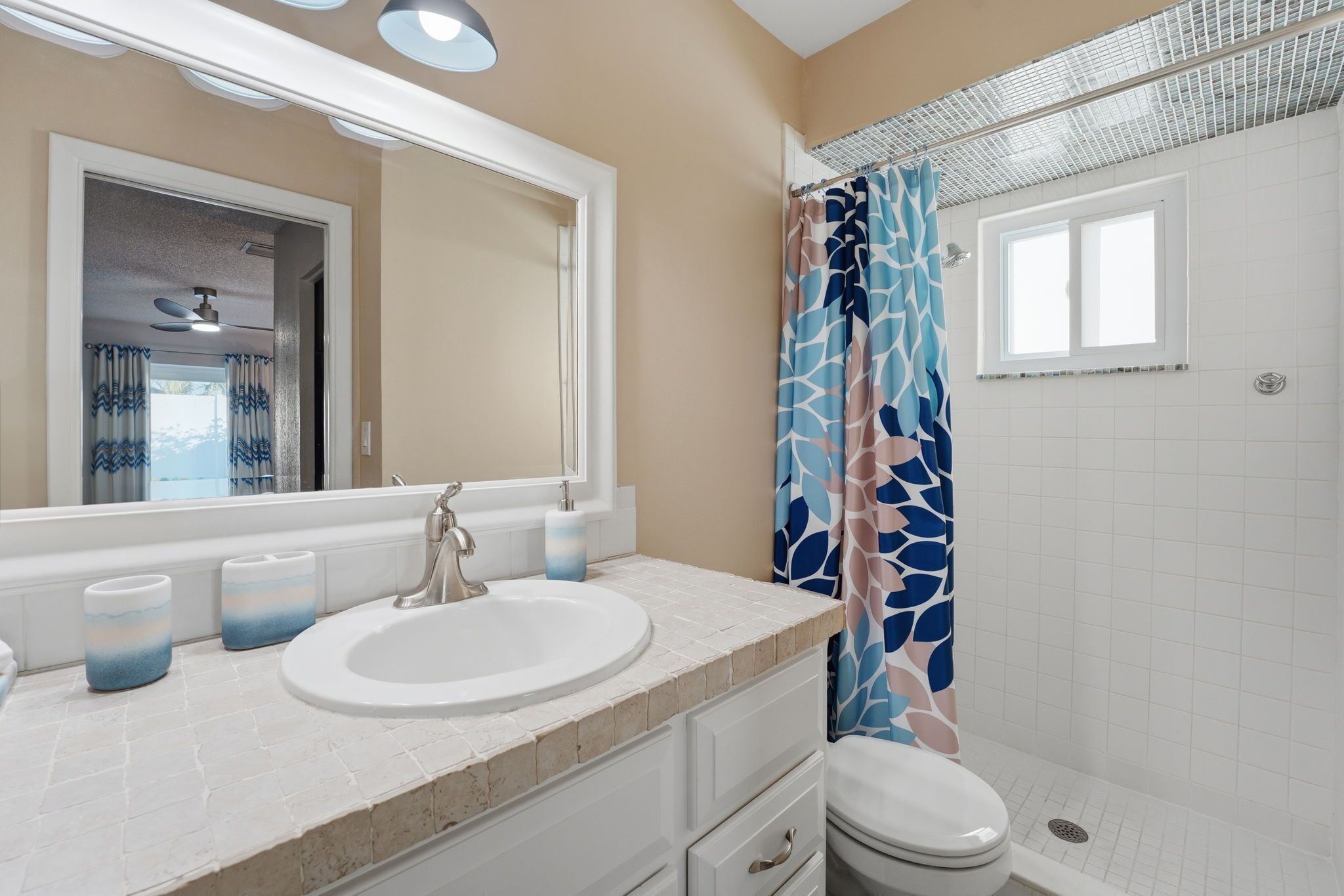 Une salle de bain avec un lavabo rond, un miroir, des toilettes et une douche avec un rideau à motifs.