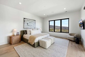 Ein Schlafzimmer mit einem großen Bett, einem Nachttisch, Blick durch ein Fenster und einem Gemälde an der Wand.