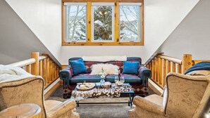 Una habitació acollidora amb un sofà, cadires, una taula amb begudes i un gran finestral amb vista a arbres.