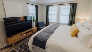 A hotel room with a bed, a TV, a chair, and a window with curtains. - Centrally Located King Bed Midtown Liberty 2695 UP (Memphis)