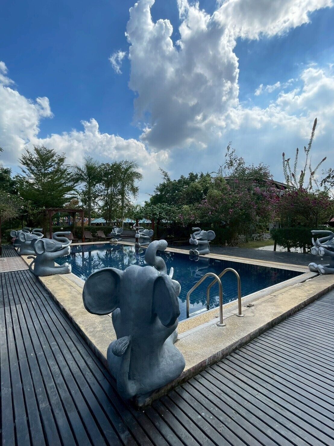 A pool area with elephant-shaped sculptures, a wooden deck, and a clear blue sky with clouds.