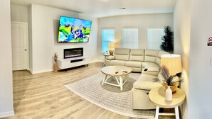 Una sala de estar con una televisión de pantalla plana, un sofá color beige, una mesa de centro y una lámpara.