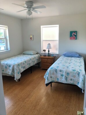 A bedroom with two single beds, a ceiling fan, a window with a view, and a nightstand with a lamp. - Harbor Delight on the Bay - All the modern amenities plus a Private Sandy Beach! (Norfolk)