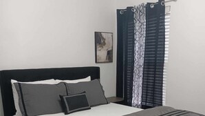 Een net opgemaakt bed met een zwart hoofdeinde, grijze beddengoed en een grijze plaid.
