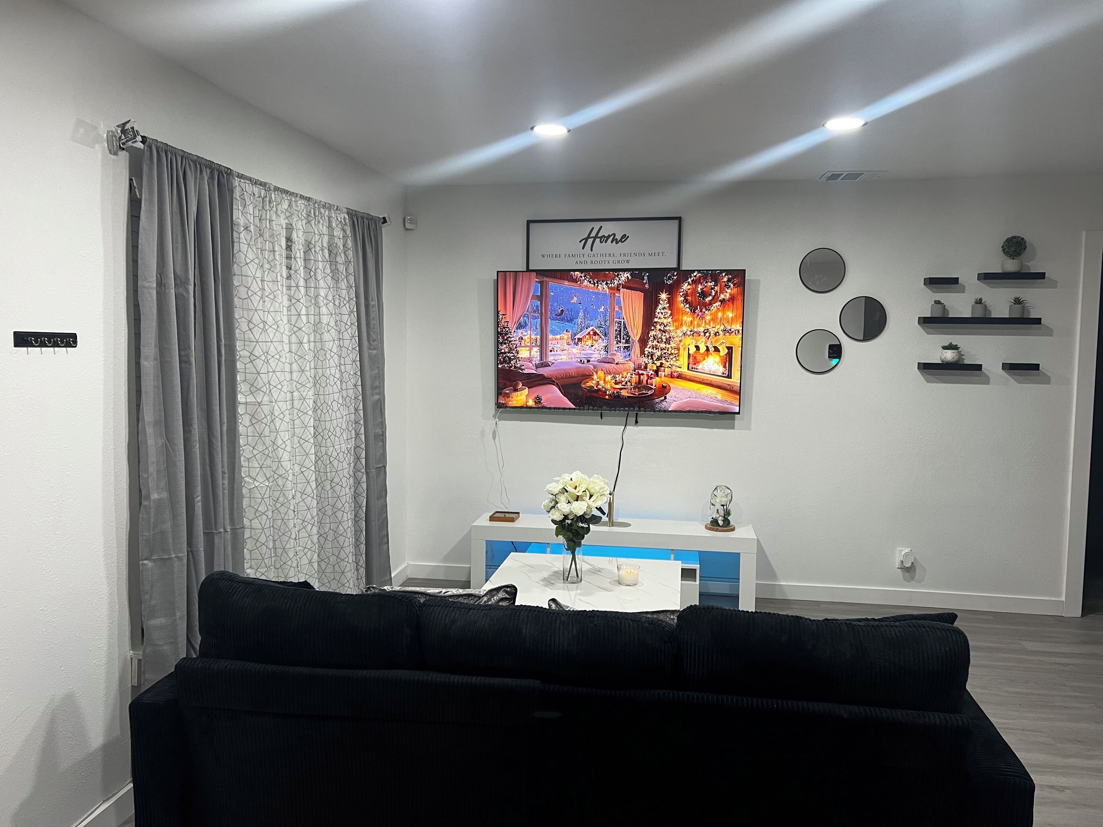 Un salon avec un canapé noir, un téléviseur fixé au mur et une cheminée.