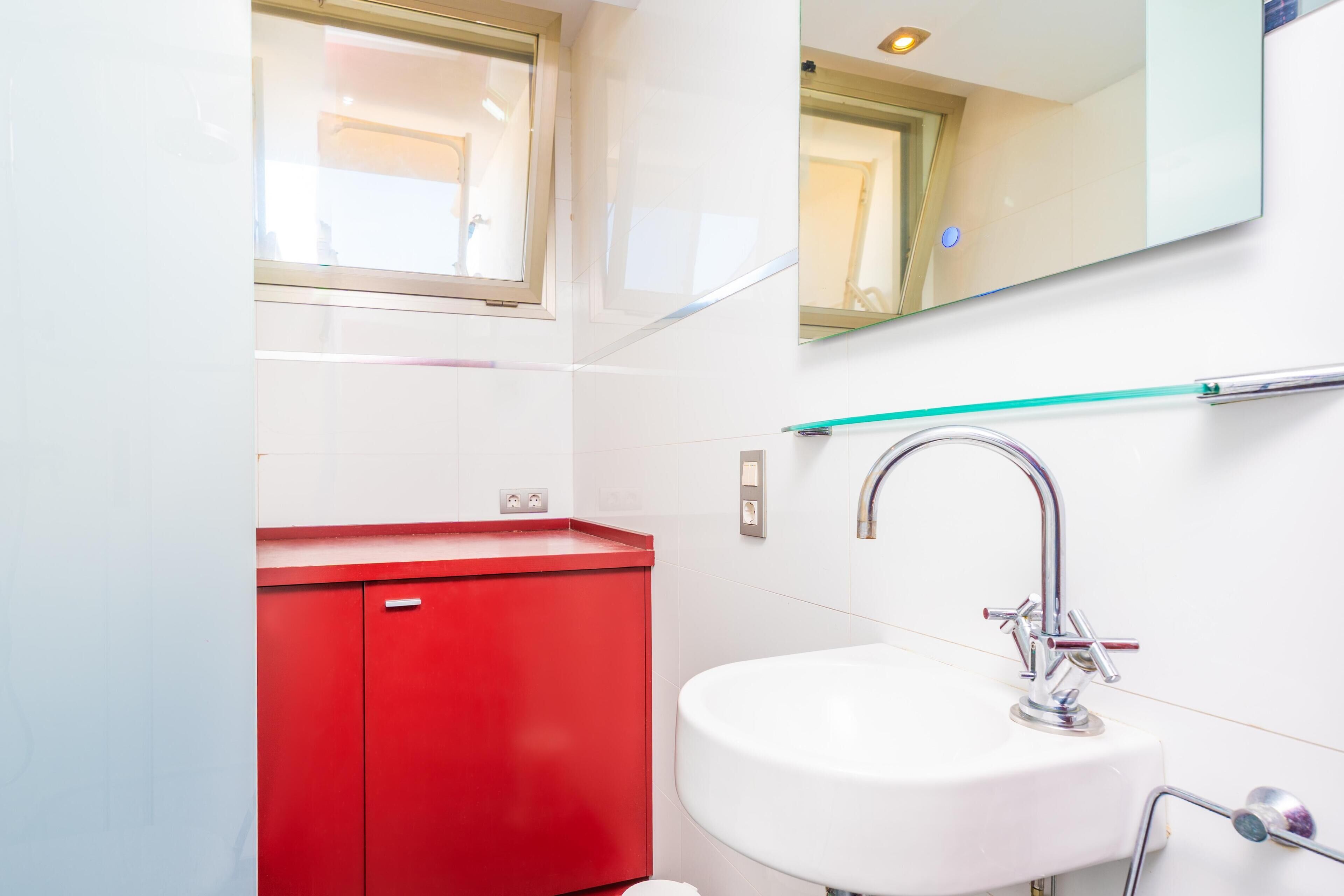 A bathroom with a white sink, red cabinet, and a mirror above the sink.