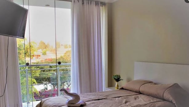 A bedroom with a bed, a TV, and a balcony with curtains.