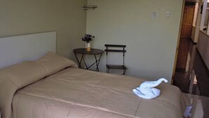 A bedroom with a bed, a small table with a vase, and a chair.