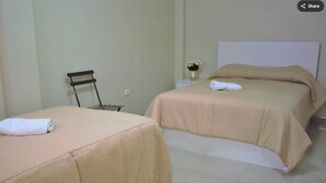 Two single beds with beige bedding, a small chair, and a nightstand with a vase of flowers.