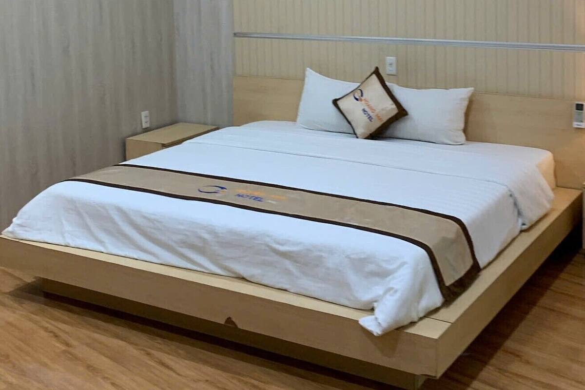 Habitación de hotel con una cama individual, suelo de madera y pared lisa con un interruptor de luz.