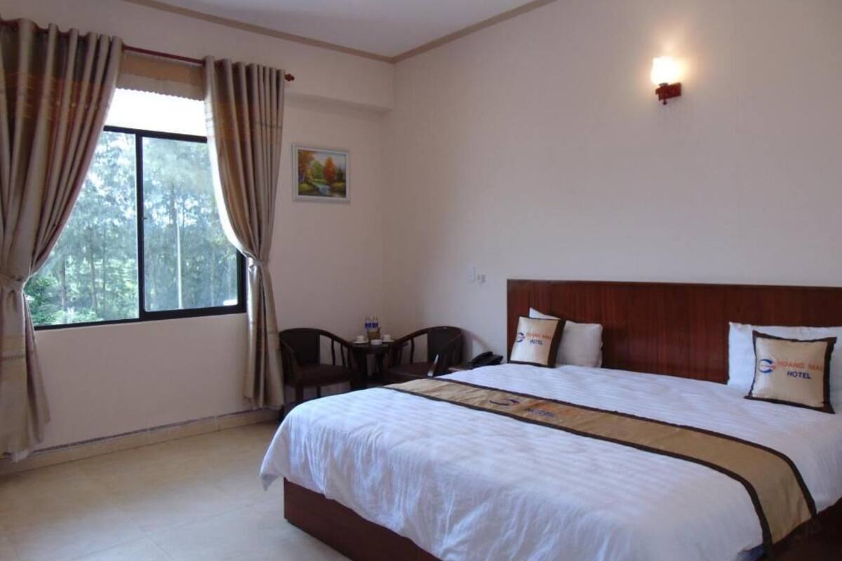 Una habitación de hotel con una cama grande, un escritorio con silla, una ventana con cortinas y un cuadro en la pared.
