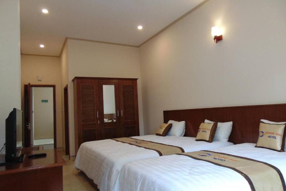 Habitación de hotel con dos camas, un armario de madera, un escritorio con televisor y una lámpara fijada a la pared.