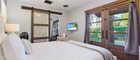 Un dormitorio con cama, televisor, puerta corredera y vistas a zonas verdes.