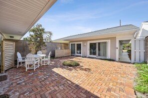 Ein Patio mit Backsteinboden, weißen Stühlen und einem kleinen Tisch.