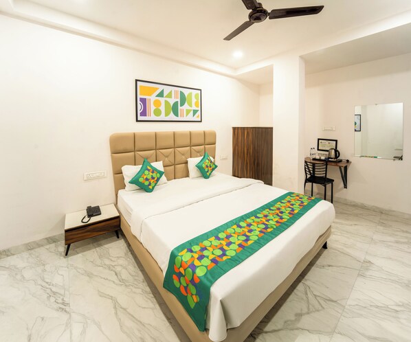 A hotel room with a bed, a desk, a chair, a ceiling fan, a mirror, and a painting on the wall. - Treebo Shridhar Stay, 2.6 Km From Indore Junction (Indore)