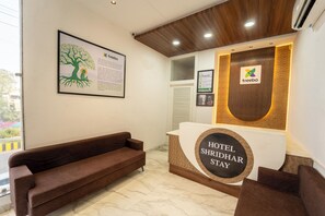 A hotel reception area with a brown sofa, a reception desk displaying the hotel's name, and a framed informational poster on the wall. - Treebo Shridhar Stay, 2.6 Km From Indore Junction (Indore)