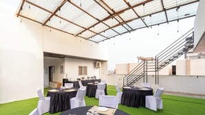 An outdoor event space with round tables, white chairs, and a covered area with a metal roof. - Treebo Shridhar Stay, 2.6 Km From Indore Junction (Indore)