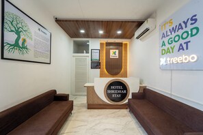 Un mostrador de recepción de hotel con un letrero que dice "HOTEL SHRIDHAR STAY" y una obra de arte con motivos de árboles en la pared.