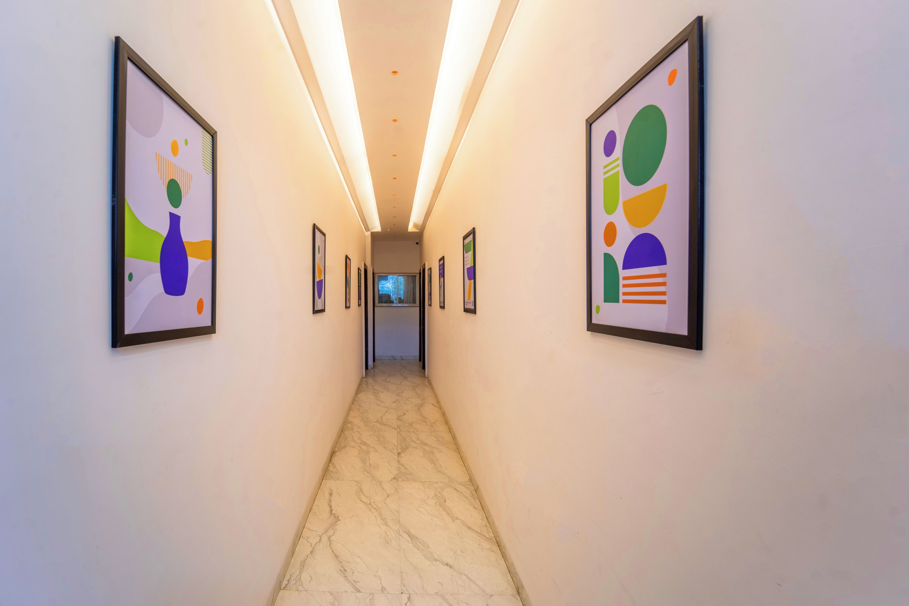 A hallway with framed abstract art on the walls and a marble floor.