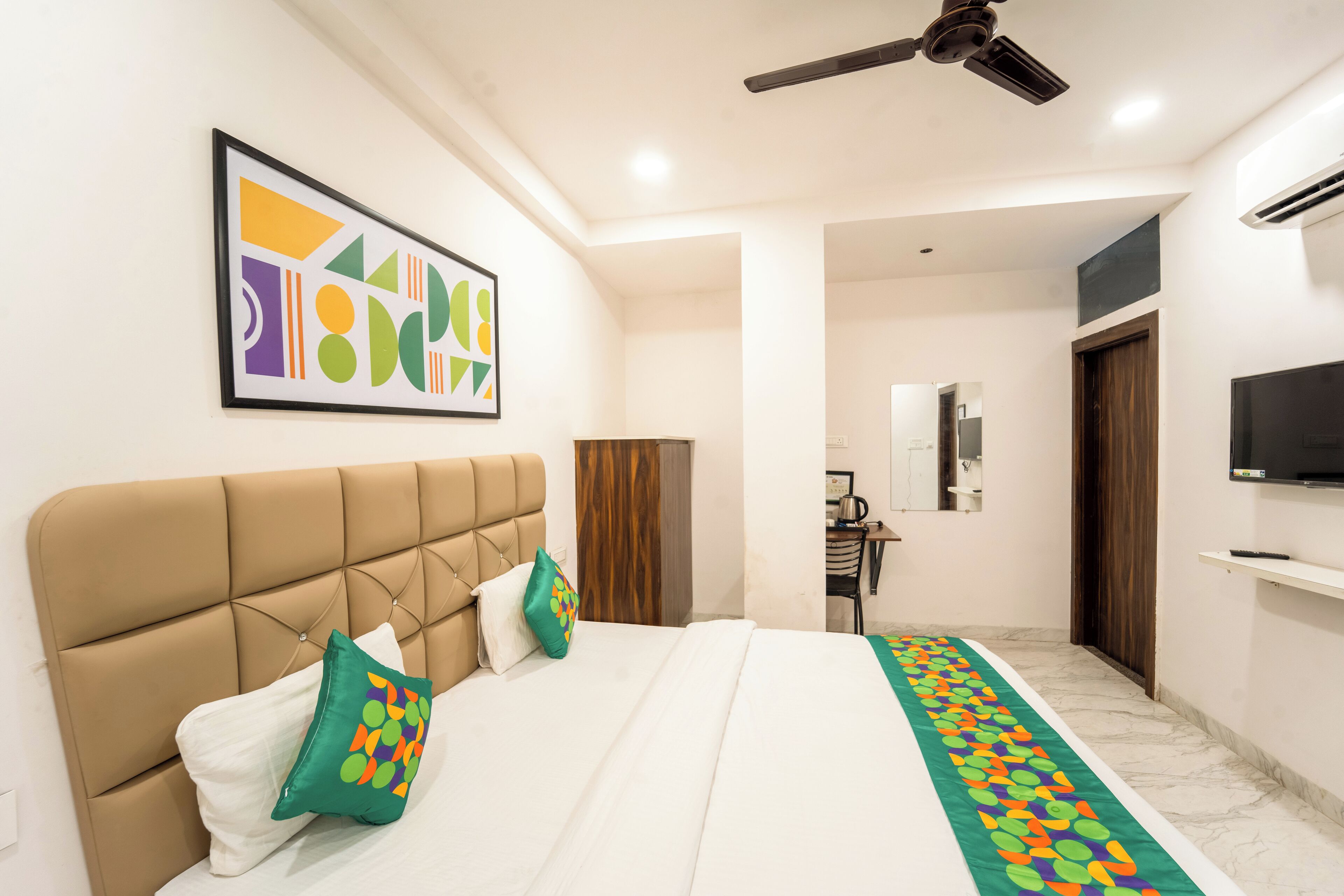 A hotel room with a large bed, a ceiling fan, a TV, and a bathroom visible in the background.