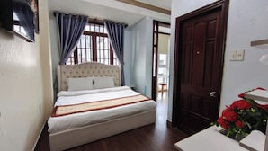 Une chambre à coucher avec un grand lit, une porte en bois et une petite table sur laquelle est posé un vase de fleurs.