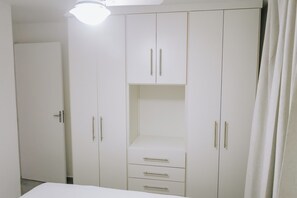 Ein weißer Kleiderschrank mit zwei Türen und einer Ablage, eine geschlossene Tür links und ein Vorhang rechts.