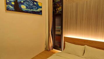 A hotel room with a bed, a painting on the wall, a window with curtains, and a wooden headboard.