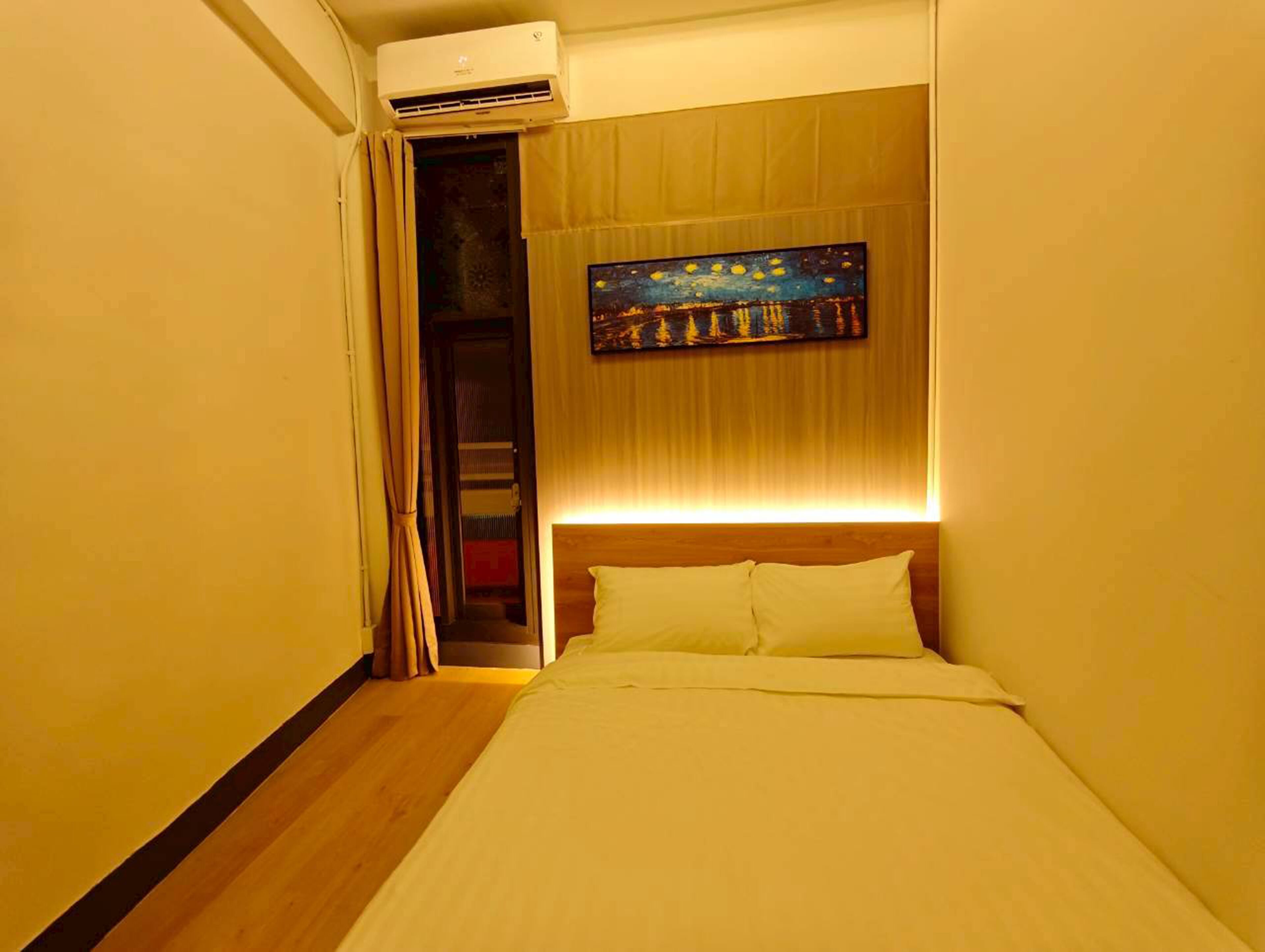 A hotel room with a bed, an air conditioning unit, a painting on the wall, and a door leading to a closet.