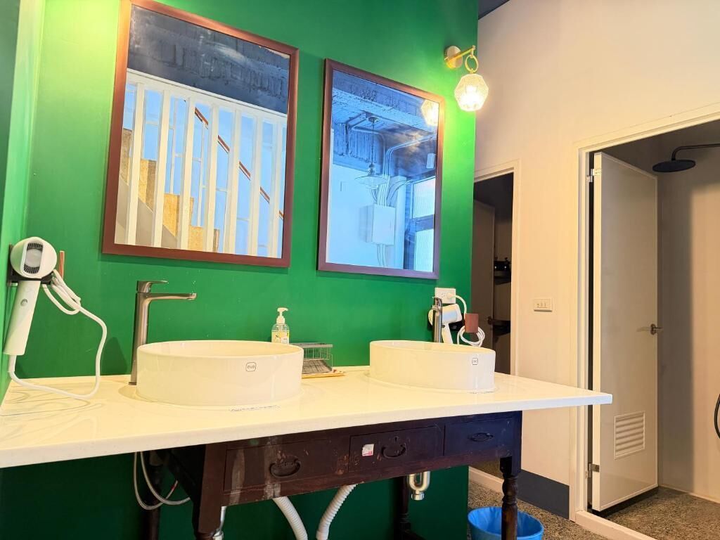 Un baño con dos lavamanos, un espejo y una pared verde.