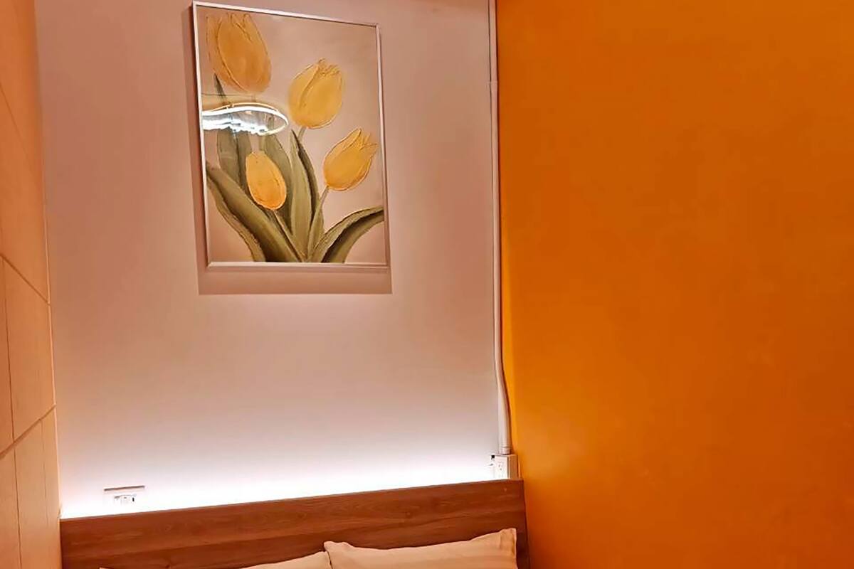 Ein Schlafzimmer mit einem Bett, einem Kopfteil, einem Wandbild mit Tulpen und einer Deckenleuchte.