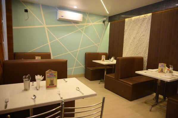A restaurant with booths and tables, some with menus and cutlery. - Hotel Sinchula (Alipurduar)