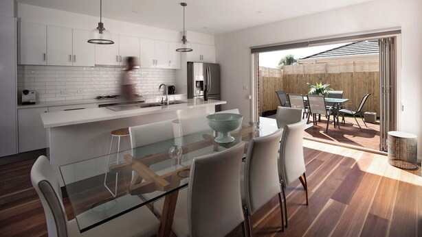A modern kitchen with white cabinets, a glass dining table, and a view of the backyard through a sliding glass door.