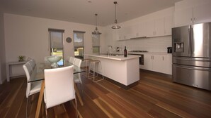 A modern kitchen with a central island, stainless steel appliances, and a dining area with glass tables and chairs.