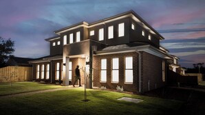 A modern two-story house with a well-lit front entrance and a visible backyard.