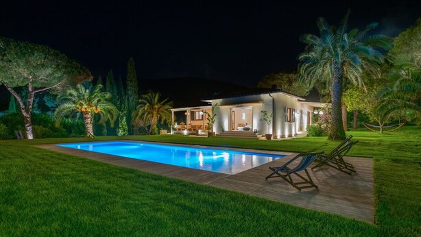 Une maison moderne dotée d’une piscine, entourée d’une végétation luxuriante et de palmiers.