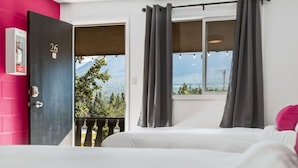 Habitació amb un llit, una finestra amb cortines, una porta amb un número i vista a arbres i muntanyes.