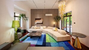 Un salon moderne avec un canapé d’angle, une table basse et une grande fenêtre donnant sur un paysage verdoyant.