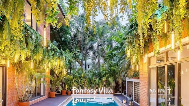 Une piscine entourée d’une végétation luxuriante et de plantes en pot, avec une pancarte indiquant : « Villa Fantaisie ».