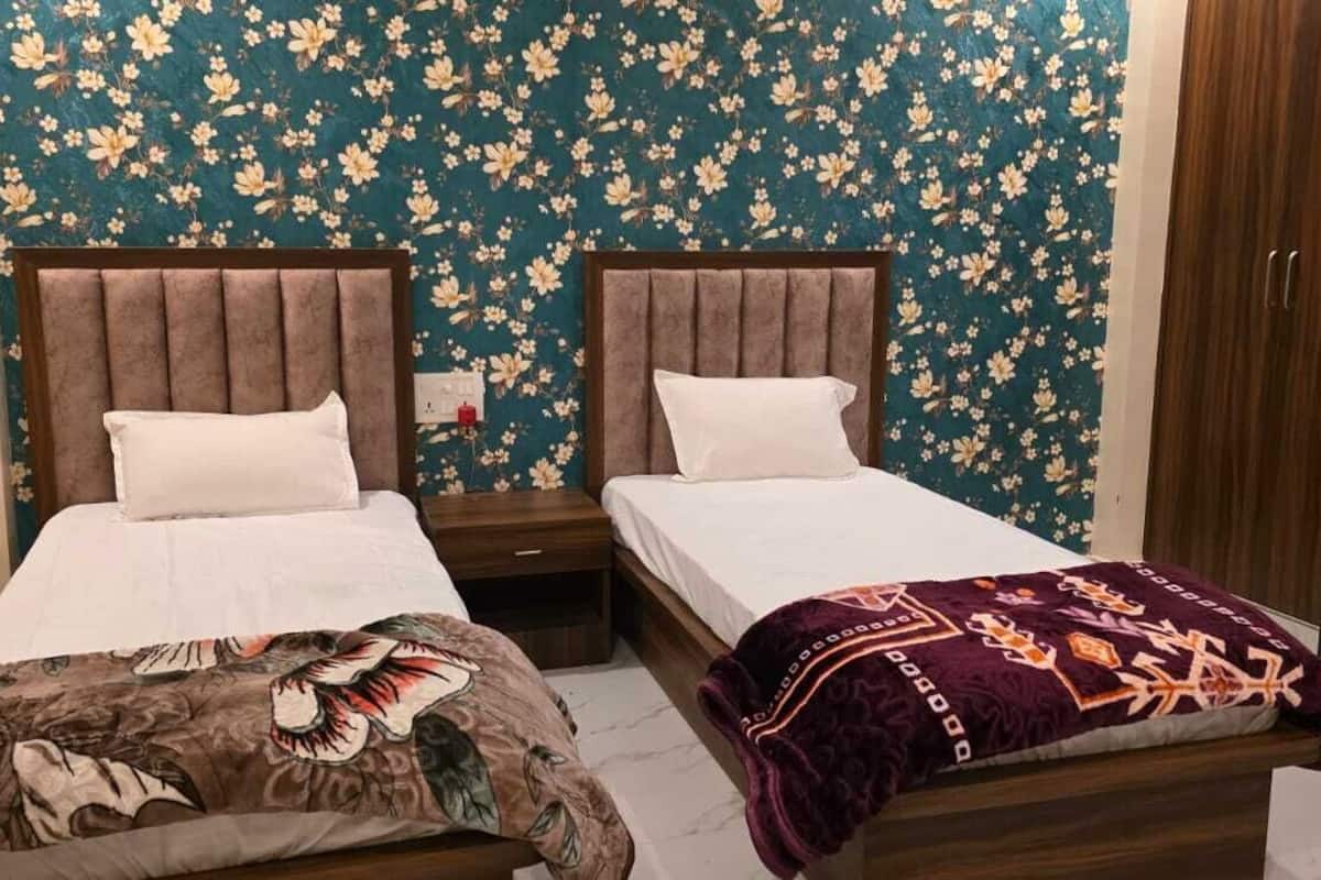 Deux lits simples avec des têtes de lit en bois et du linge de lit blanc, une couvre-lit à motifs floraux foncés sur le côté gauche et une couverture rouge foncé à motifs géométriques sur le côté droit.