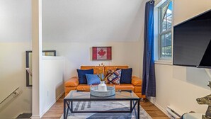 Un salon avec une table basse en verre, un canapé orange et un téléviseur fixé au mur.