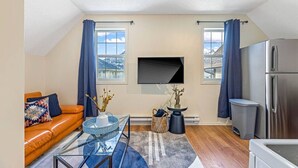 Un salon moderne avec une table basse en verre, un canapé, un téléviseur fixé au mur et un réfrigérateur.