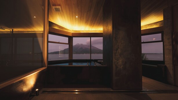 A modern interior with large windows, a wooden ceiling, and a view of a mountain and water body. - Good Fellows Resort (Kagoshima)