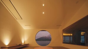 A minimalist room with a circular window overlooking a mountainous landscape. - Good Fellows Resort (Kagoshima)