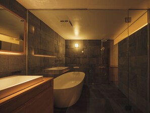 A modern bathroom with a freestanding bathtub, a large mirror, and a wall-mounted sink. - Good Fellows Resort (Kagoshima)